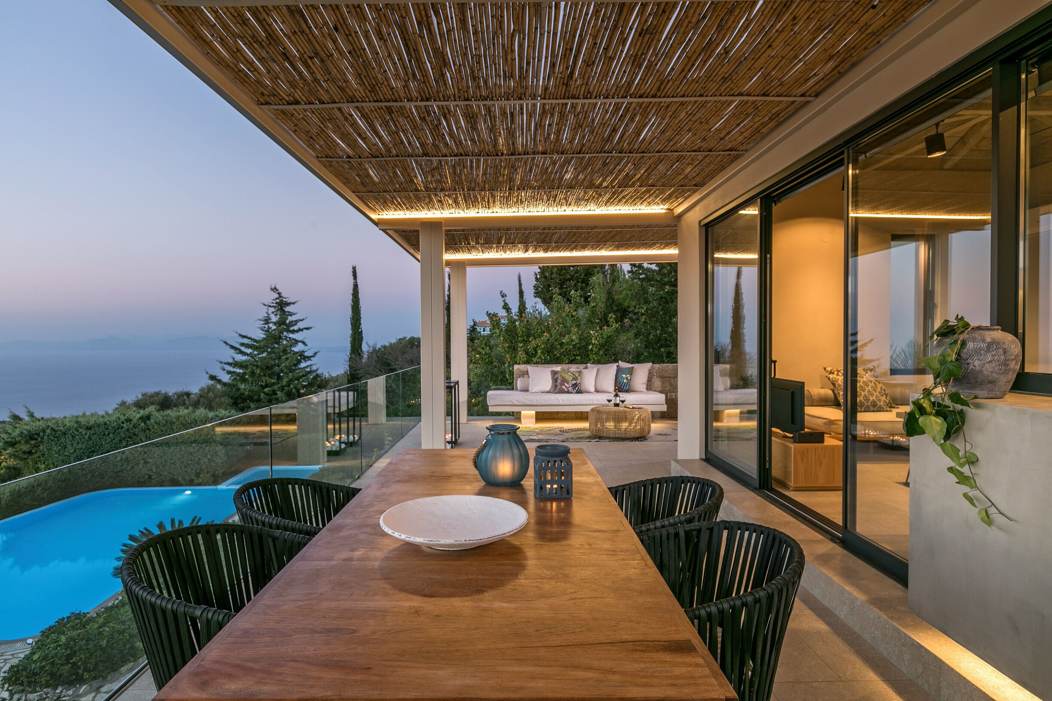 A modern outdoor dining area with a wooden table, chairs, and a view of the ocean.