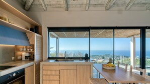A modern kitchen with a large island, a dining area with a view, and a large window overlooking the ocean. - Art Blue Villas (Lefkada)