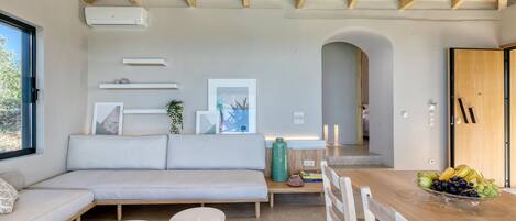 A modern interior with a wooden ceiling, a sofa, a dining table with fruit, and a view through a window.