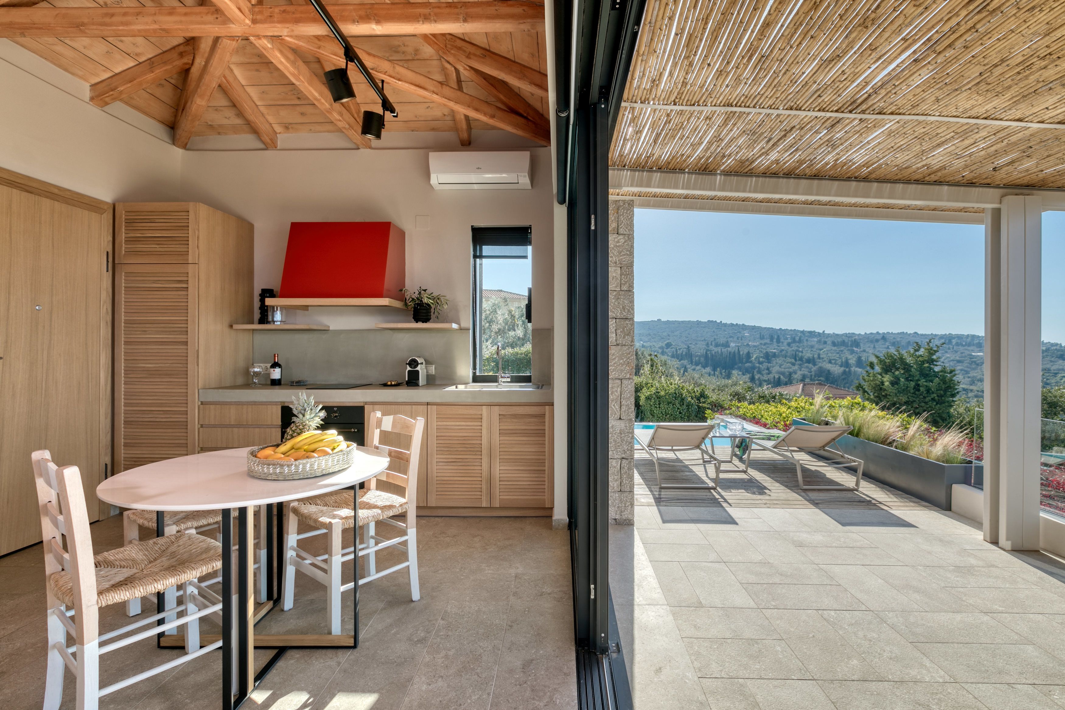 Una cocina moderna con armarios de madera, una campana extractora roja y un comedor con una mesa y sillas redondas.