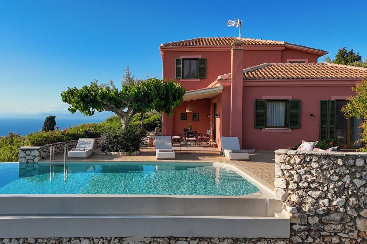 A villa with a swimming pool, outdoor seating, and a view of the sea.