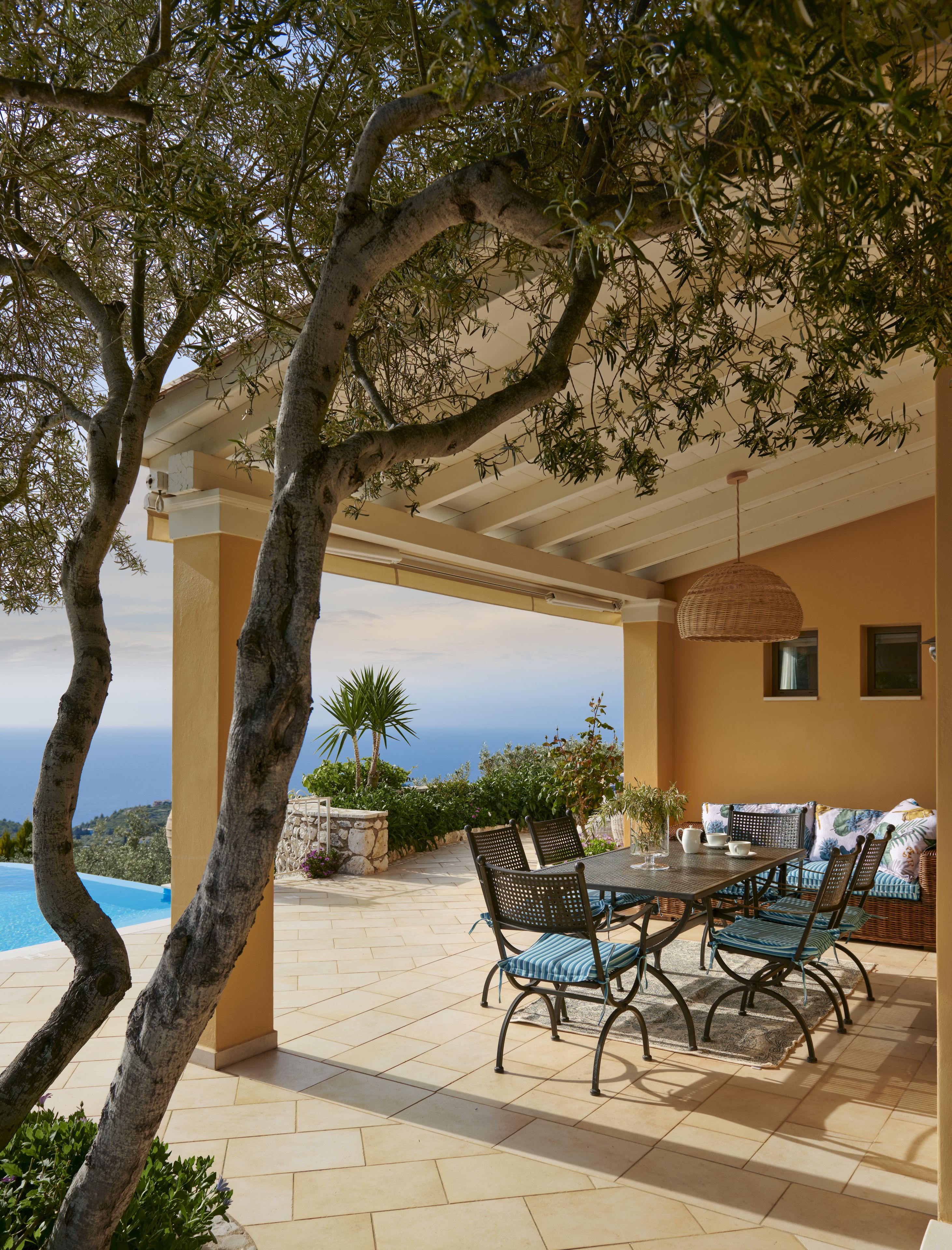 An outdoor patio with a table and chairs, a hanging light fixture, and a view of the sea.