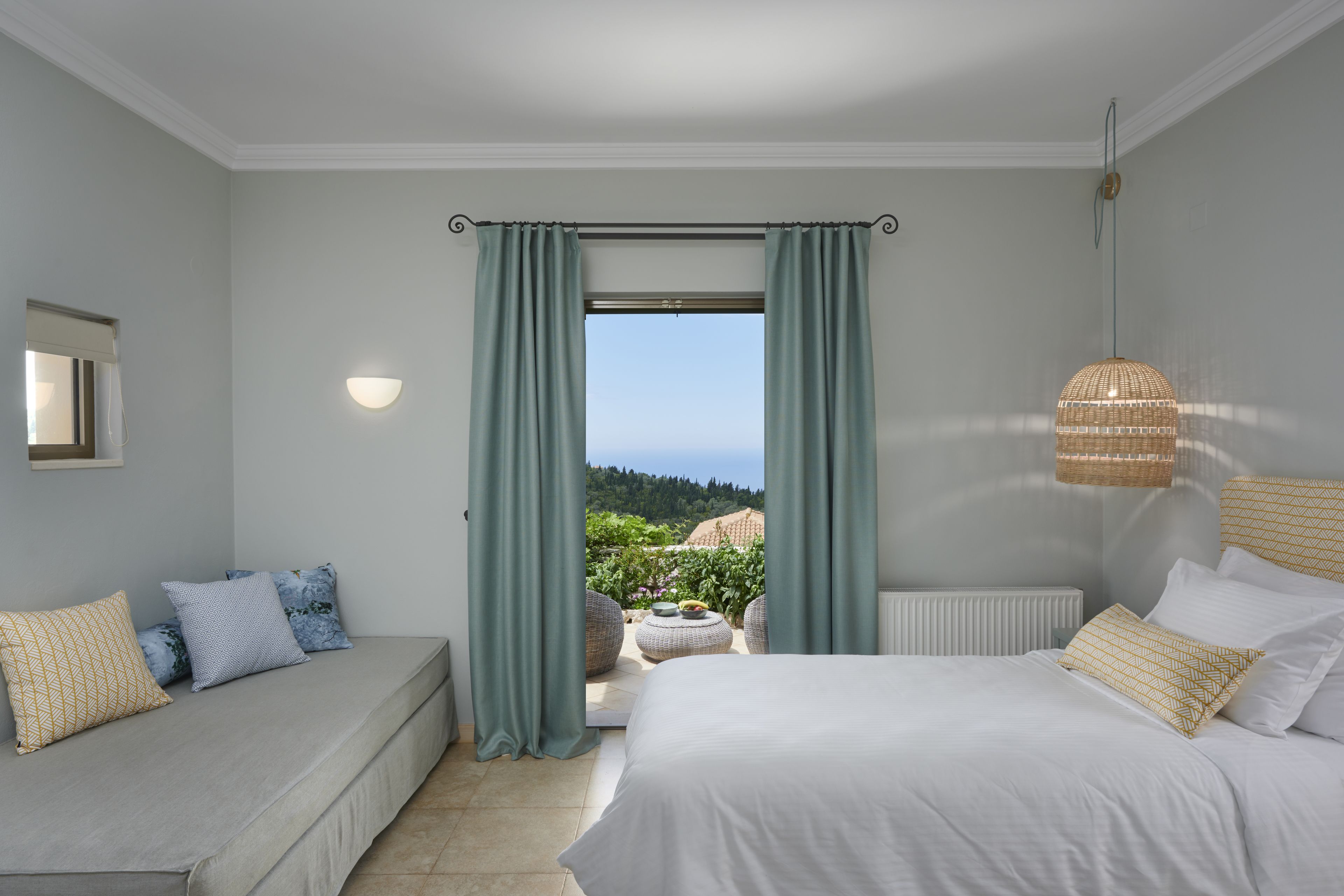 A bedroom with a bed, a sofa, and a view of a garden.