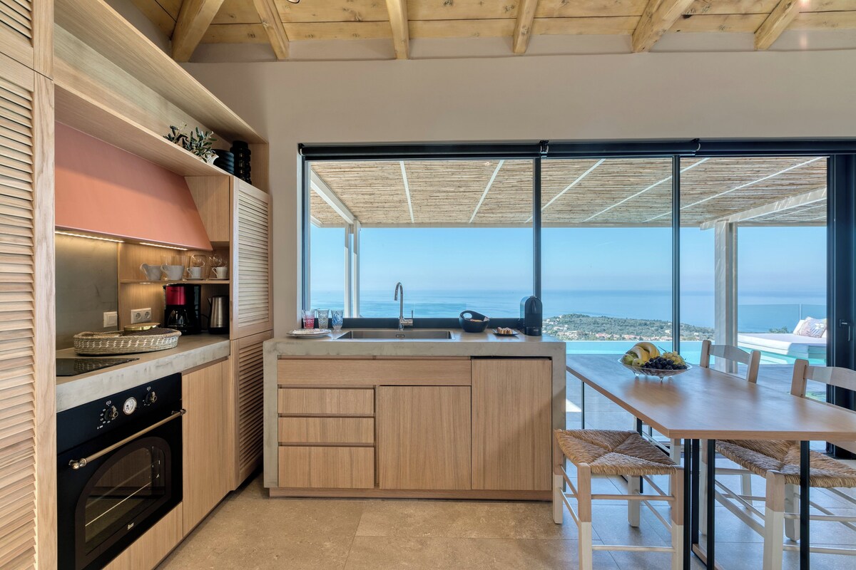 A modern kitchen with a large island, a built-in oven, and a view of the sea.