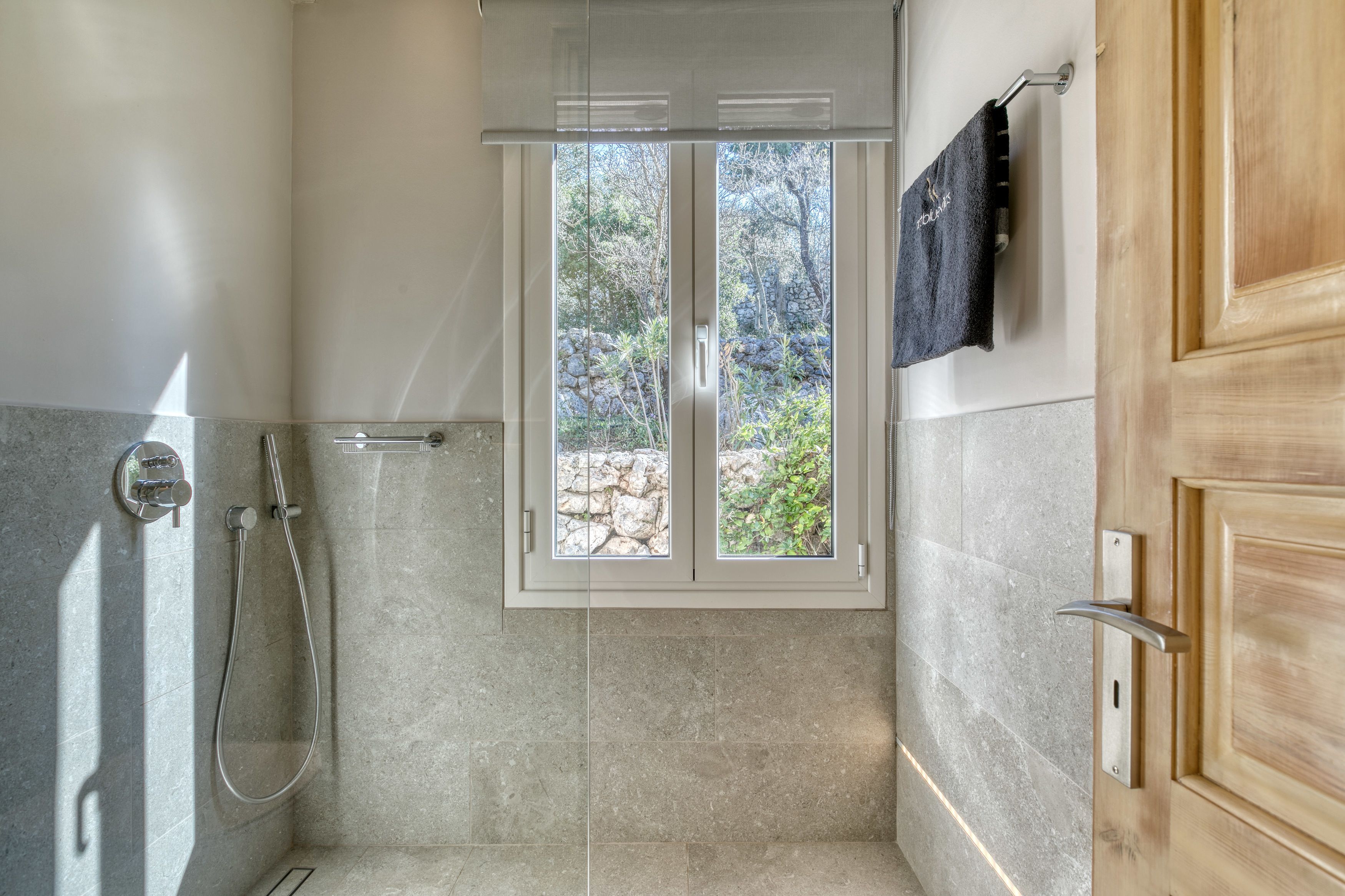 A shower with a glass door, a towel rack with a towel, and a window with a view of trees and rocks.