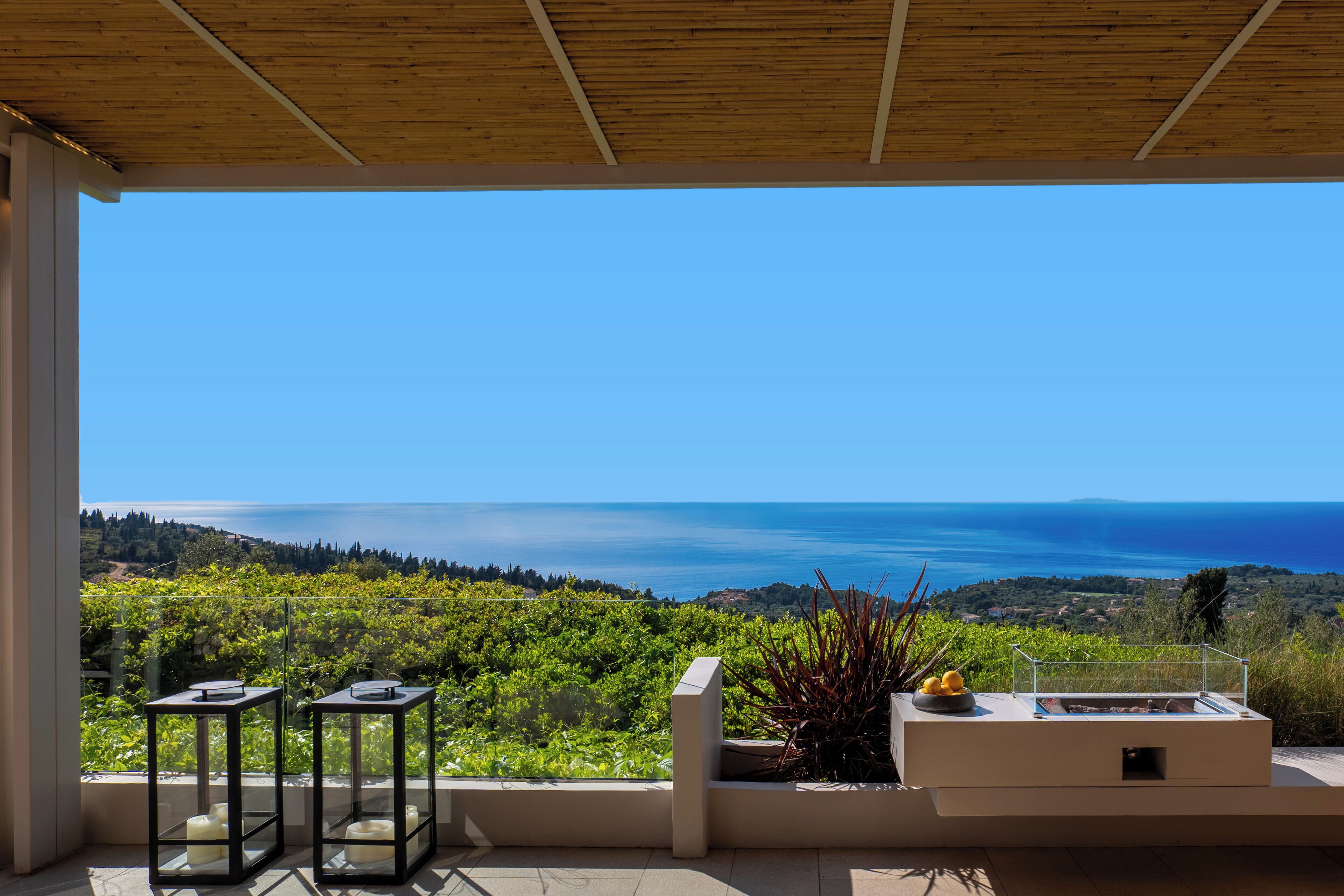 A terrace with a clear view of the sea, a wooden ceiling, and a table with candles.