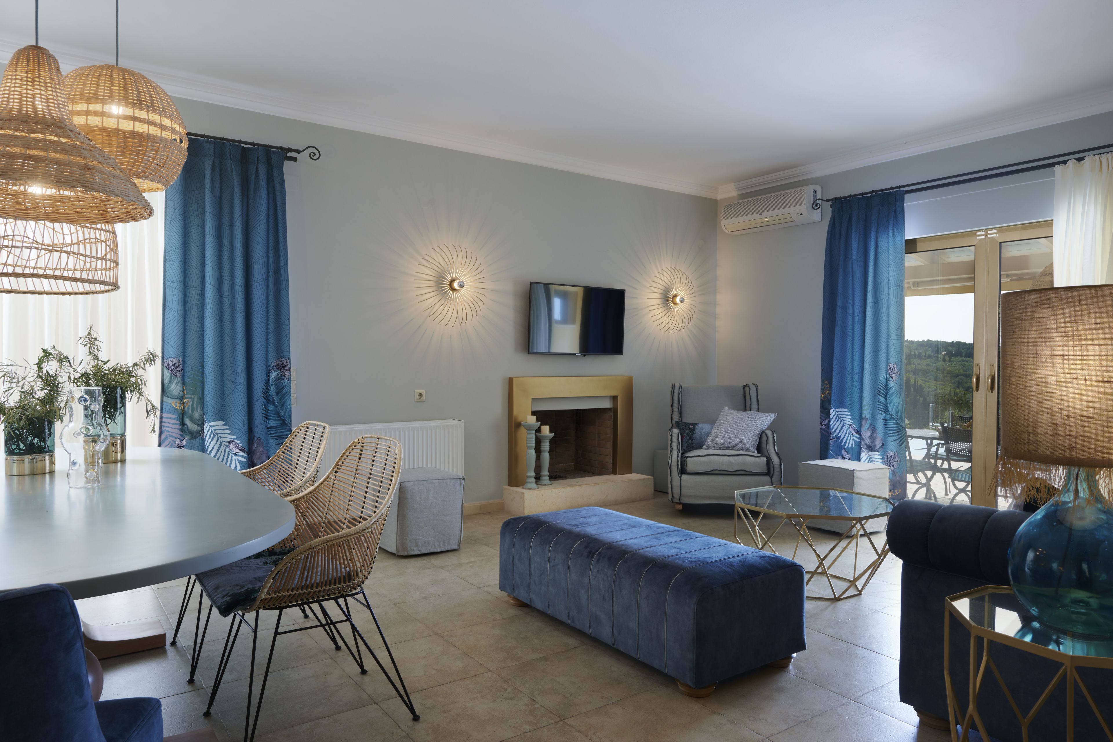 A modern living room with a round dining table, wicker chairs, a blue sofa, and a glass coffee table.