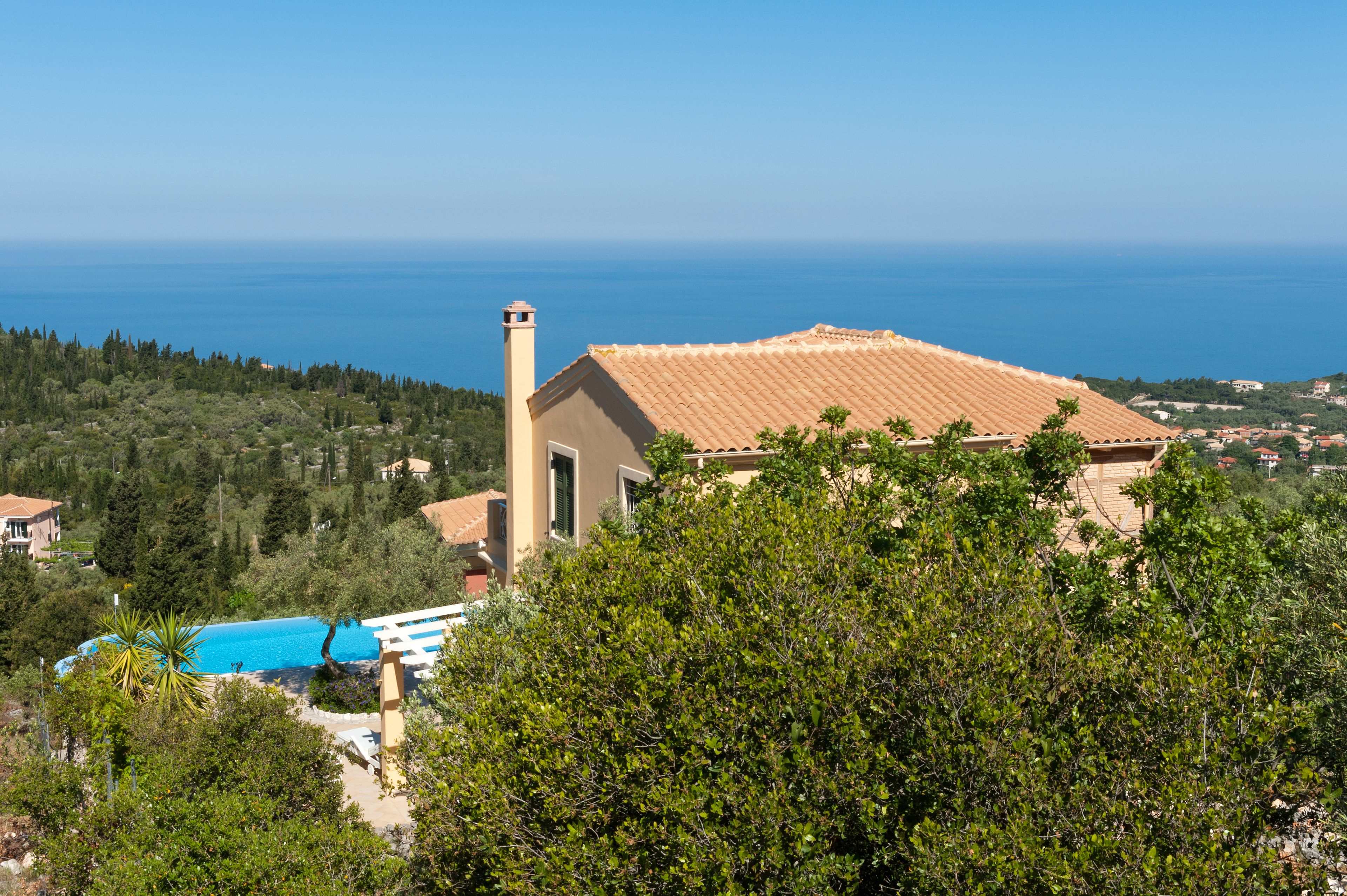 Una villa costera con techo de tejas, chimenea y vista al mar.