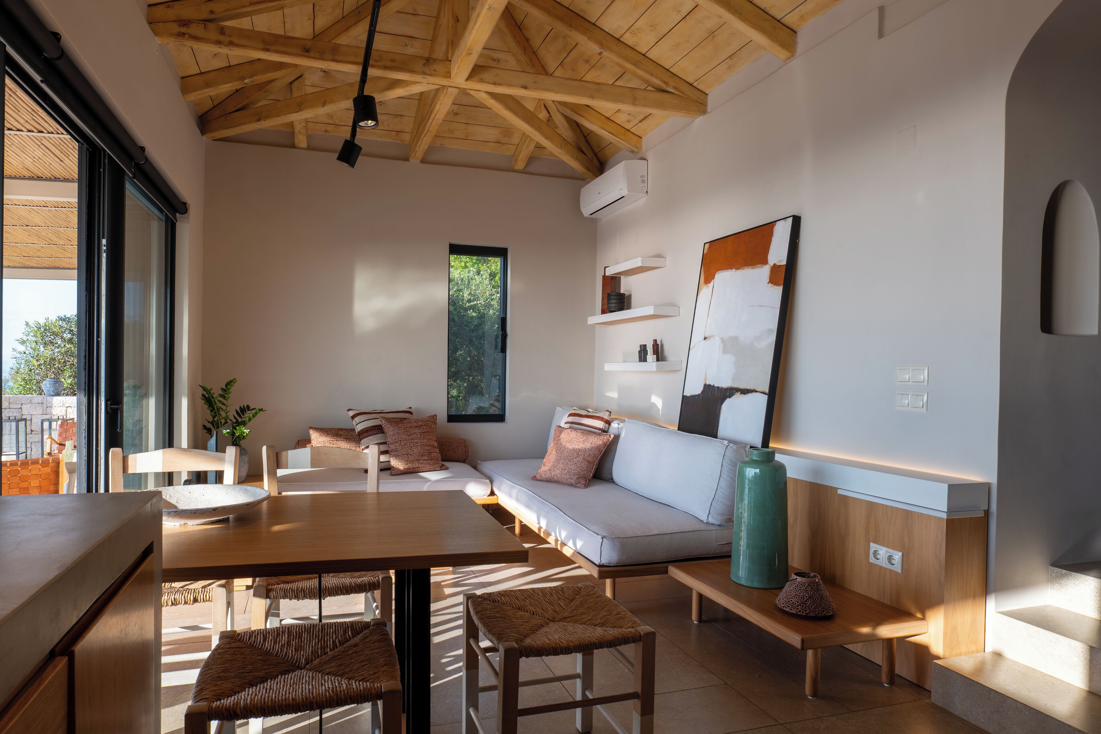 Una sala de estar moderna con techo de madera, un sofá, una mesa de comedor y un ventanal grande.