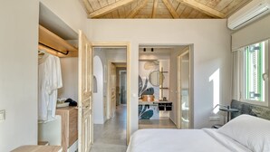 A bedroom with a large bed, wooden ceiling beams, a walk-in closet, and a bathroom with a shower and a mirror. - Art Blue Villas (Lefkada)