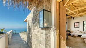 A stone exterior wall with a glass door, a wooden ceiling, a sofa, and a view of the sea. - Art Blue Villas (Lefkada)
