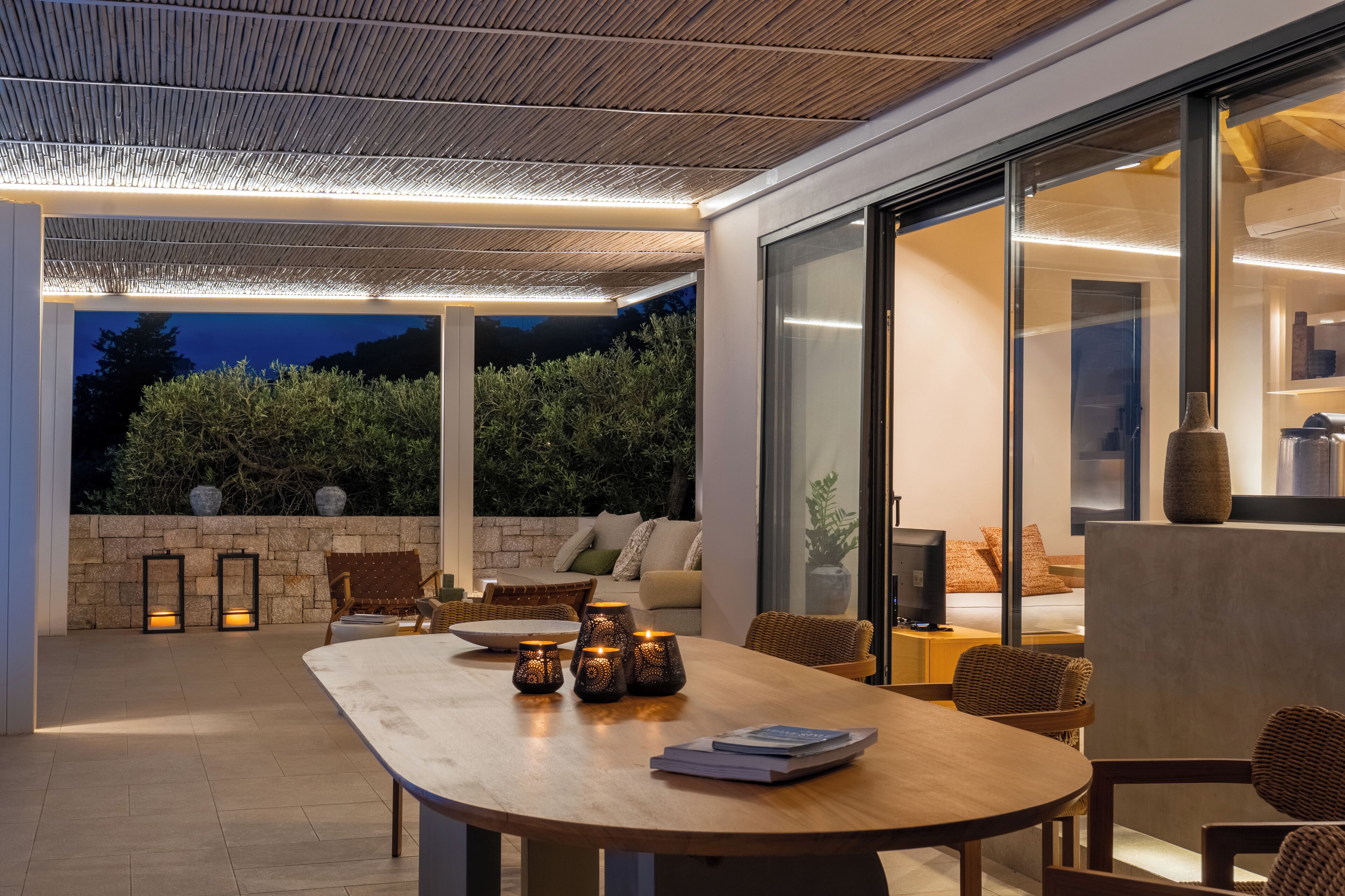 An outdoor dining area with a wooden table, wicker chairs, and candles.