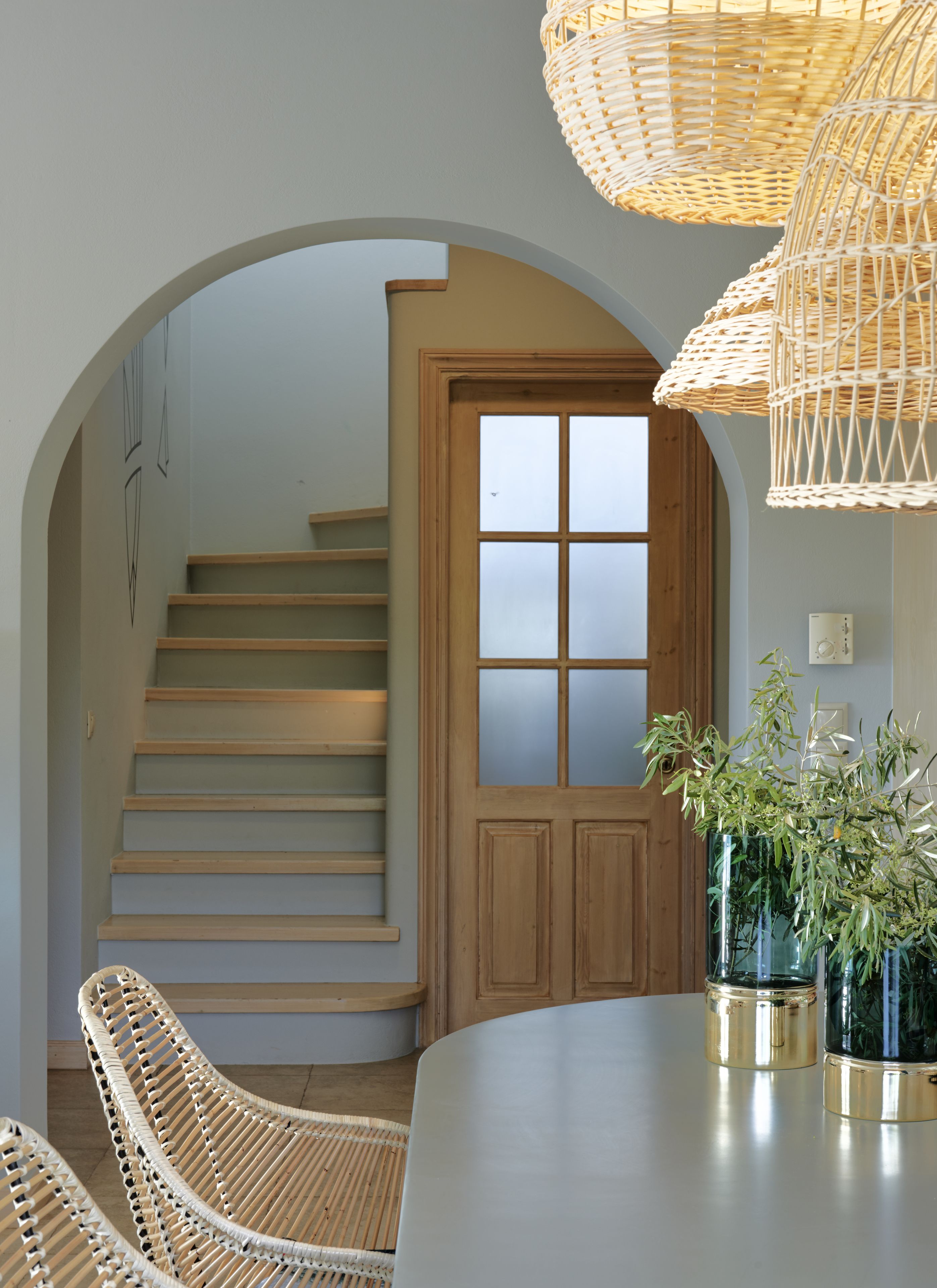 Eine Treppe mit Holzboden und einer Glastür. Korbstühle und ein Tisch mit einer Pflanze sind ebenfalls vorhanden.