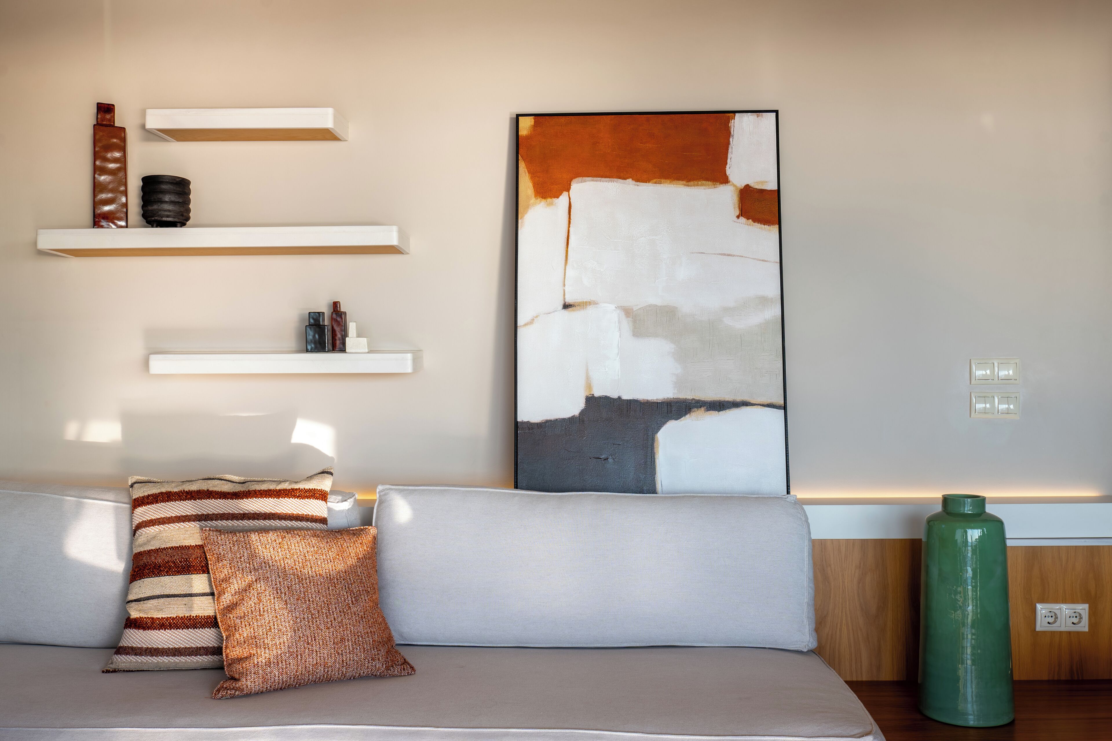 Una sala de estar moderna con un sofá gris, almohadas a rayas, un jarrón verde y arte abstracto en la pared.