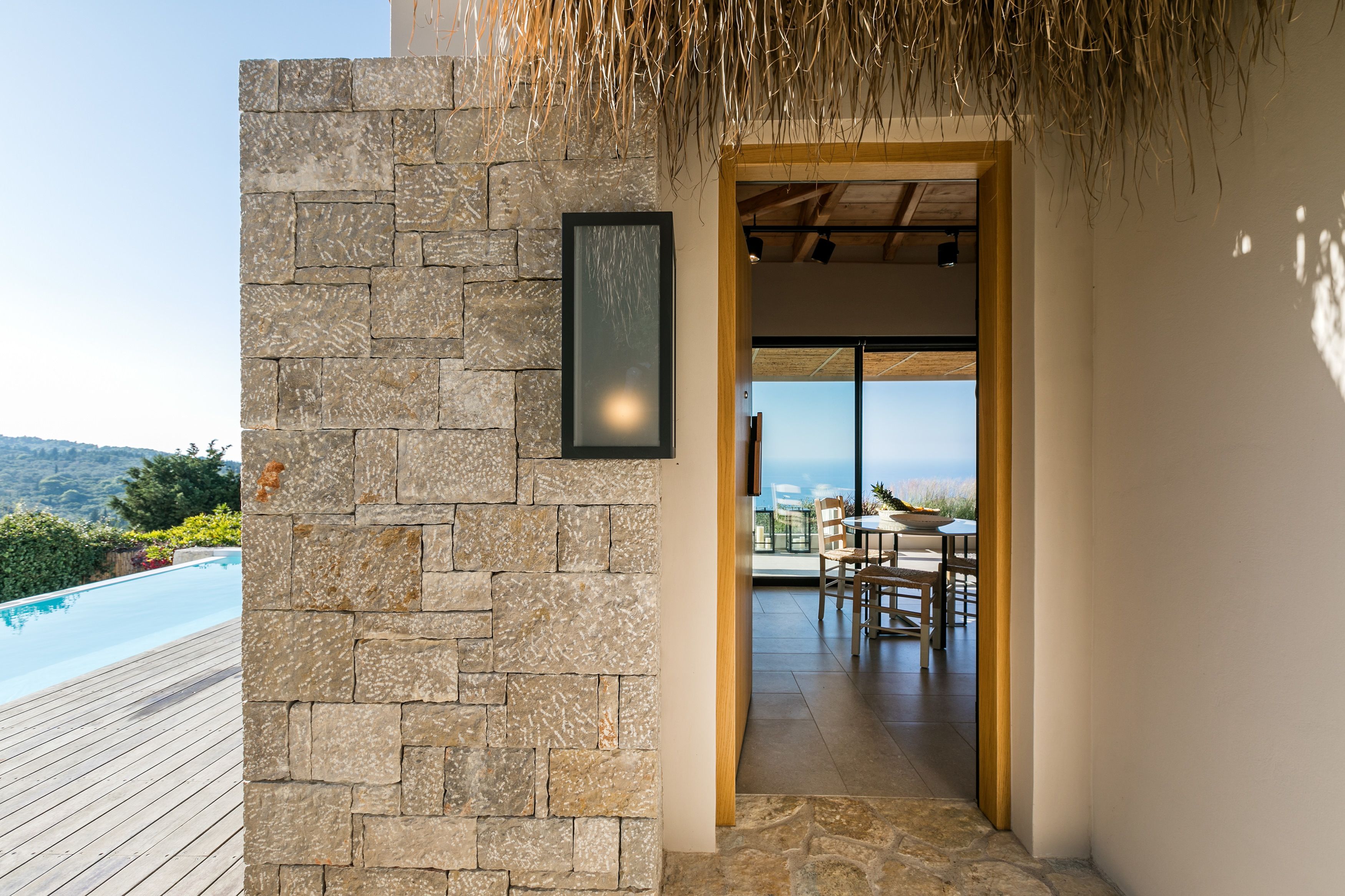 Un mur de pierre orné d’un tableau encadré, qui mène à un balcon avec un espace repas et une piscine.