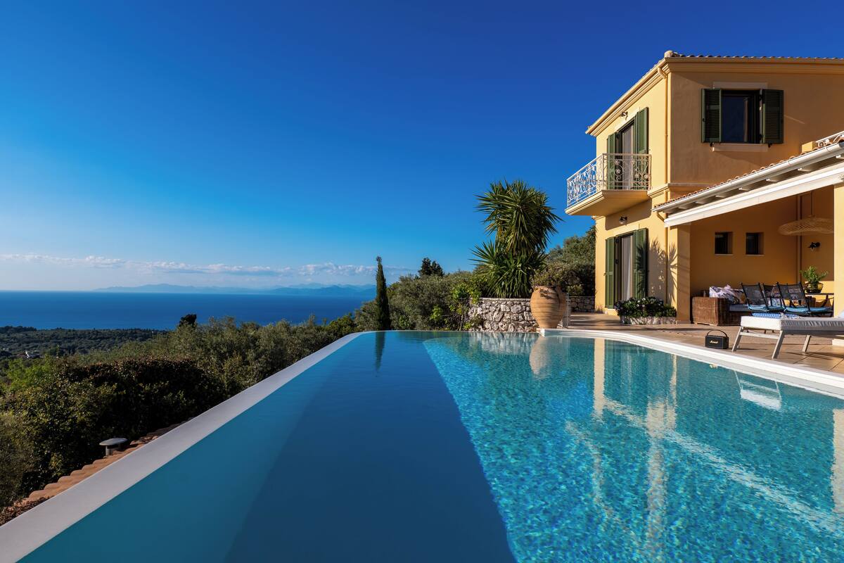 A poolside view of a Mediterranean-style villa with a clear view of the sea.