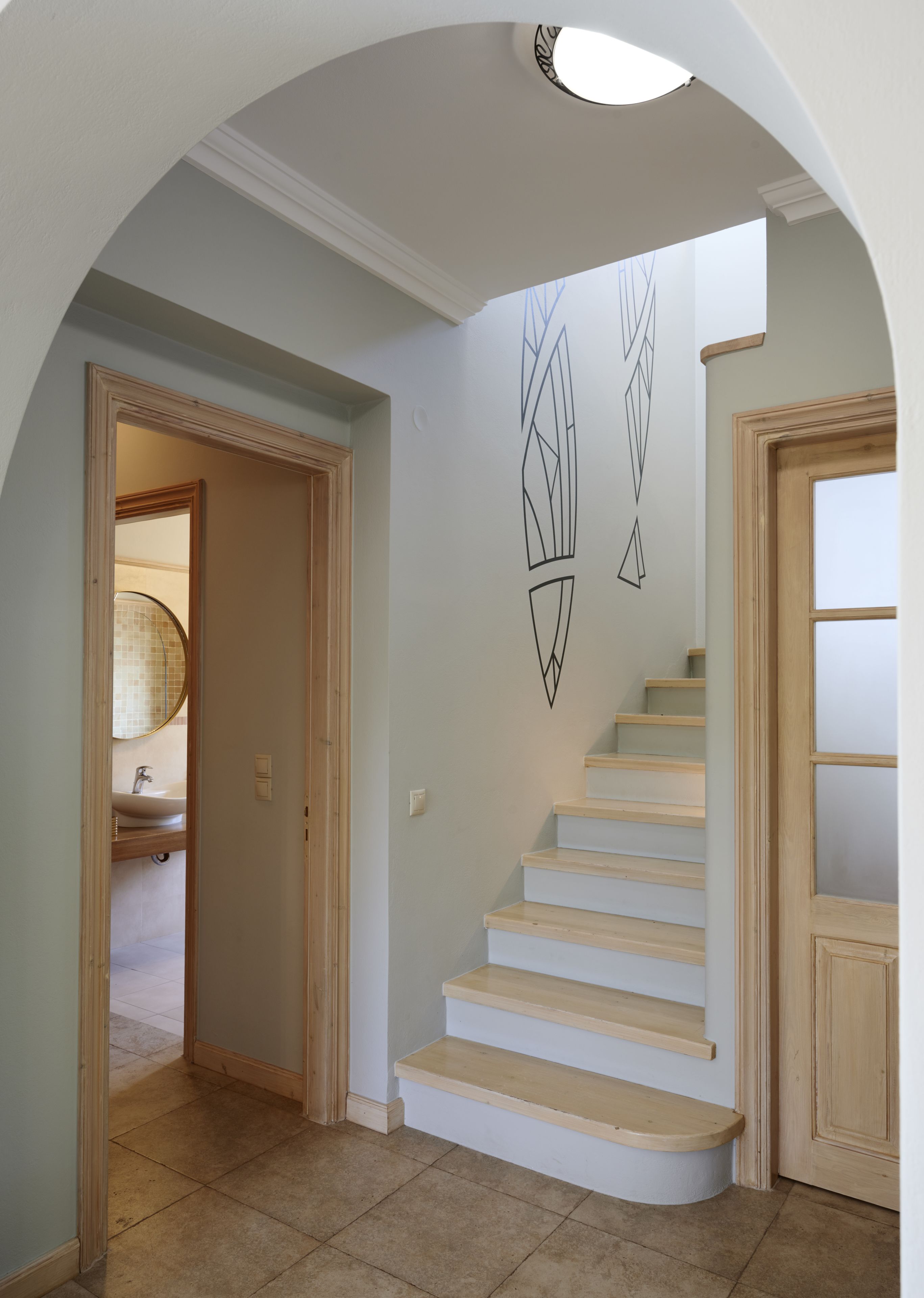 Una escalera con barandilla de color claro y peldaños, que conduce a una habitación con puerta de madera y un ventanal pequeño.