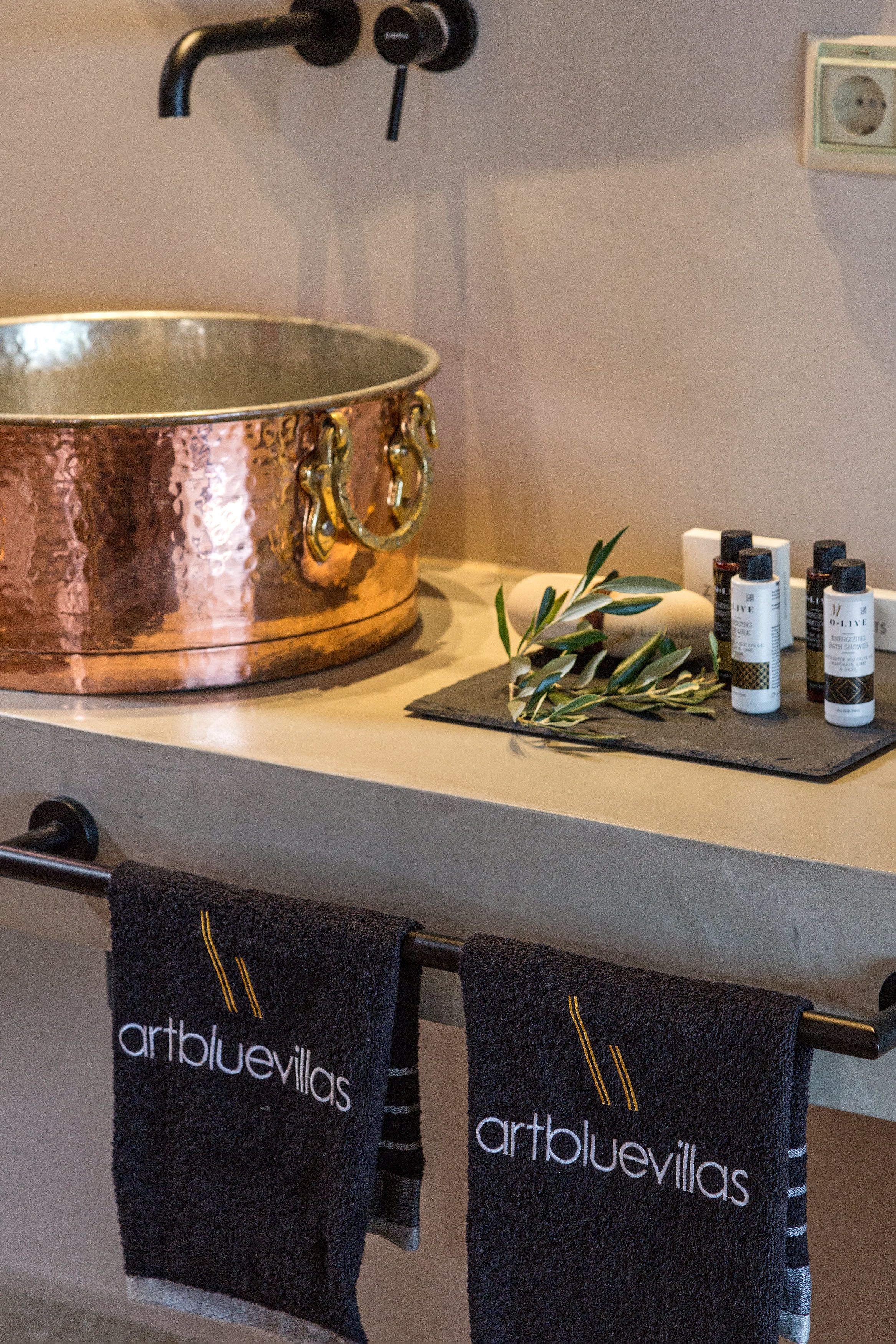 Baño con lavamanos de cobre, artículos de aseo y toallas con la marca 'artbluevillas'.