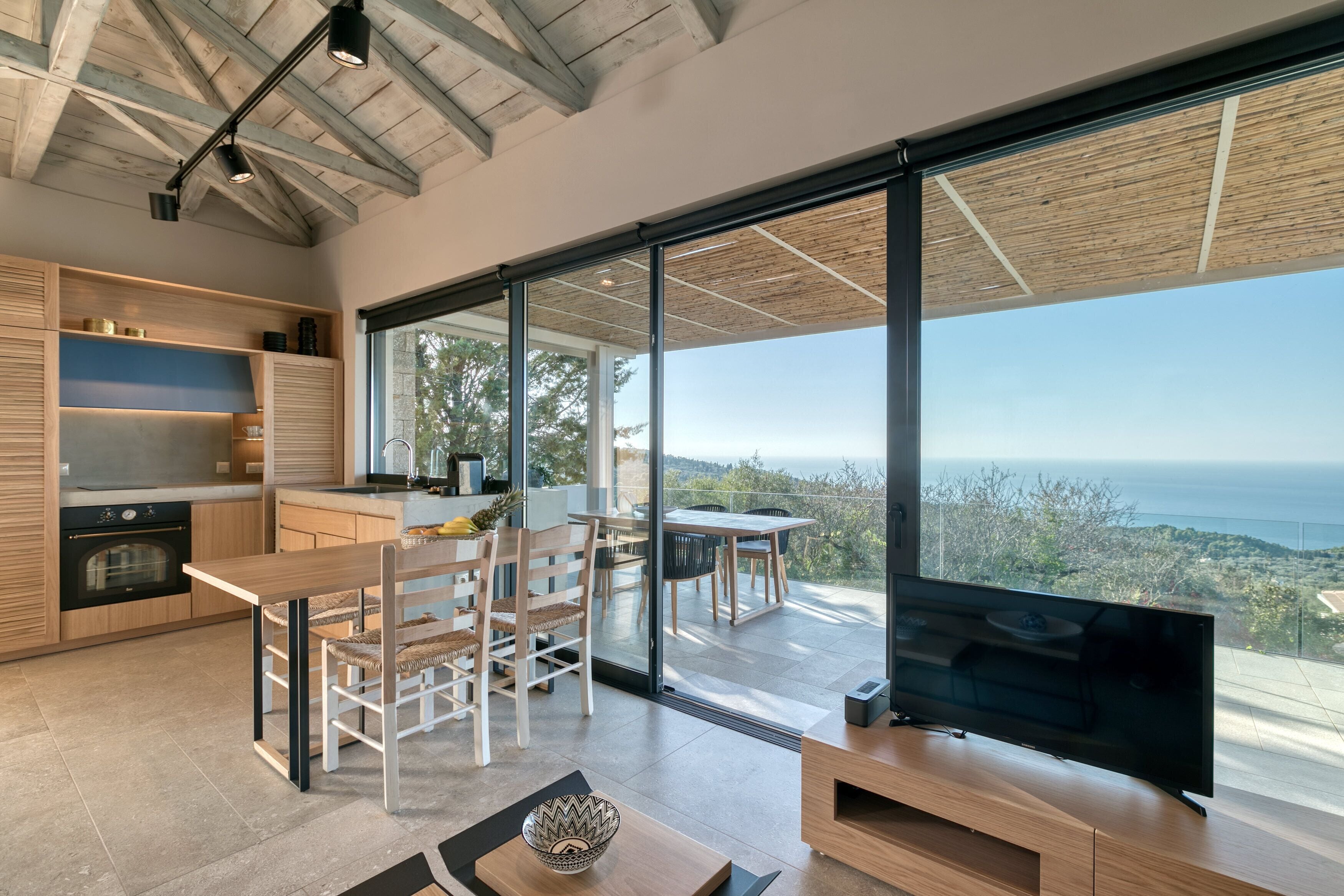 Una cocina moderna con armarios de madera, un comedor con mesa y sillas, y un amplio ventanal corredero que da a un balcón con vistas al océano.