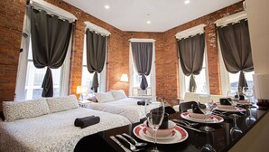 Habitación de hotel con dos camas, una mesa de comedor con platos y vasos, y una pared de ladrillo.