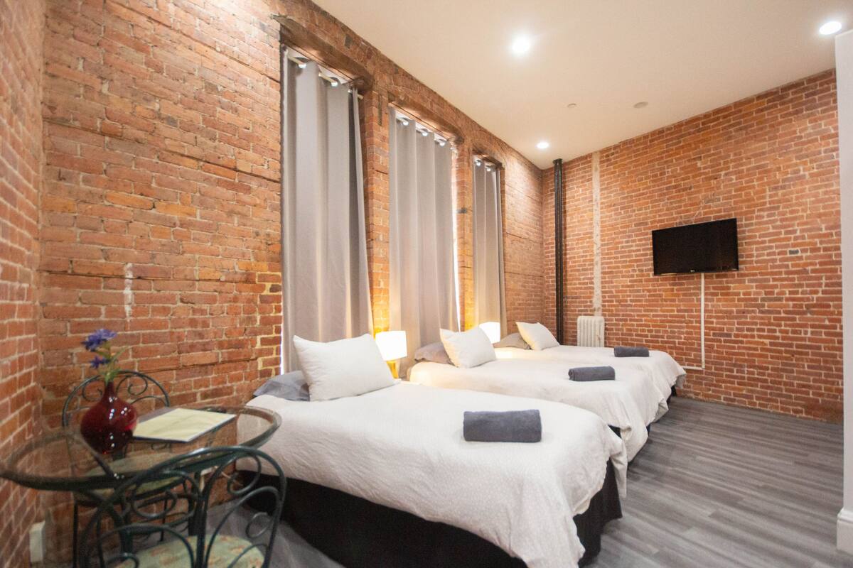 A hotel room with brick walls, two beds, a TV, and a small table with a vase.
