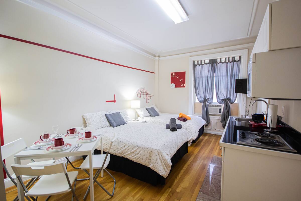 A compact hotel room with a bed, a small kitchenette, a dining area, and a bathroom.