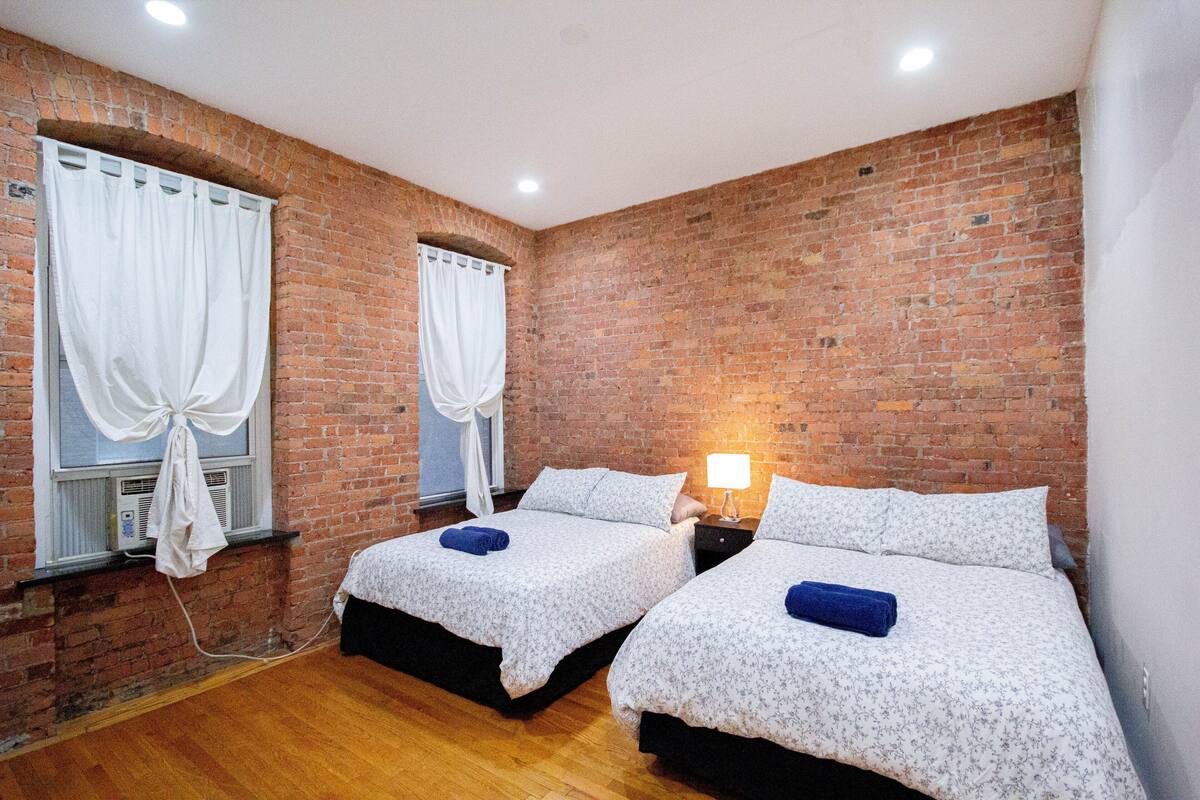 A room with two beds, a brick wall, and a window with curtains.