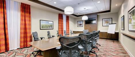 A conference room with a long table, multiple chairs, a whiteboard, and framed pictures on the walls.
