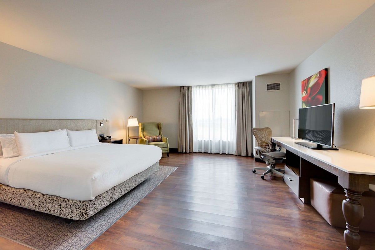 A hotel room with a large bed, a desk with a TV, a chair, and a lamp.
