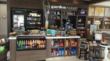 Un supermercado llamado 'The Garden Market' con secciones para alimentos congelados y refrigerados, estantes llenos de refrigerios y una máquina de café.