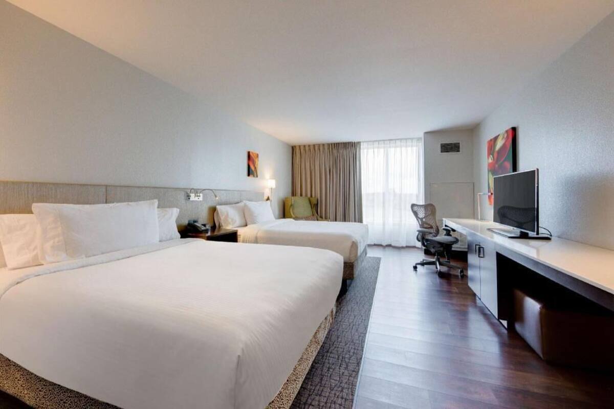 A hotel room with two beds, a desk, a chair, a television, and a window with curtains.