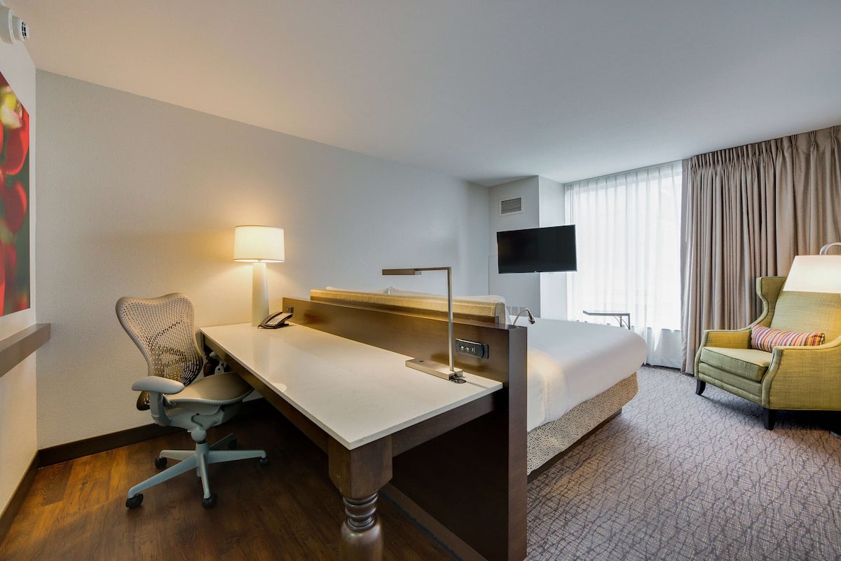 A hotel room with a desk, chair, bed, TV, and a sofa.