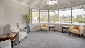 A spacious room with a high ceiling, large windows, and a seating area with two armchairs and a small table. - Quality Inn Idaho Falls (Idaho Falls)