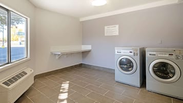 A laundry room with two washing machines, a vent, a window, and a sign indicating guest laundry services.