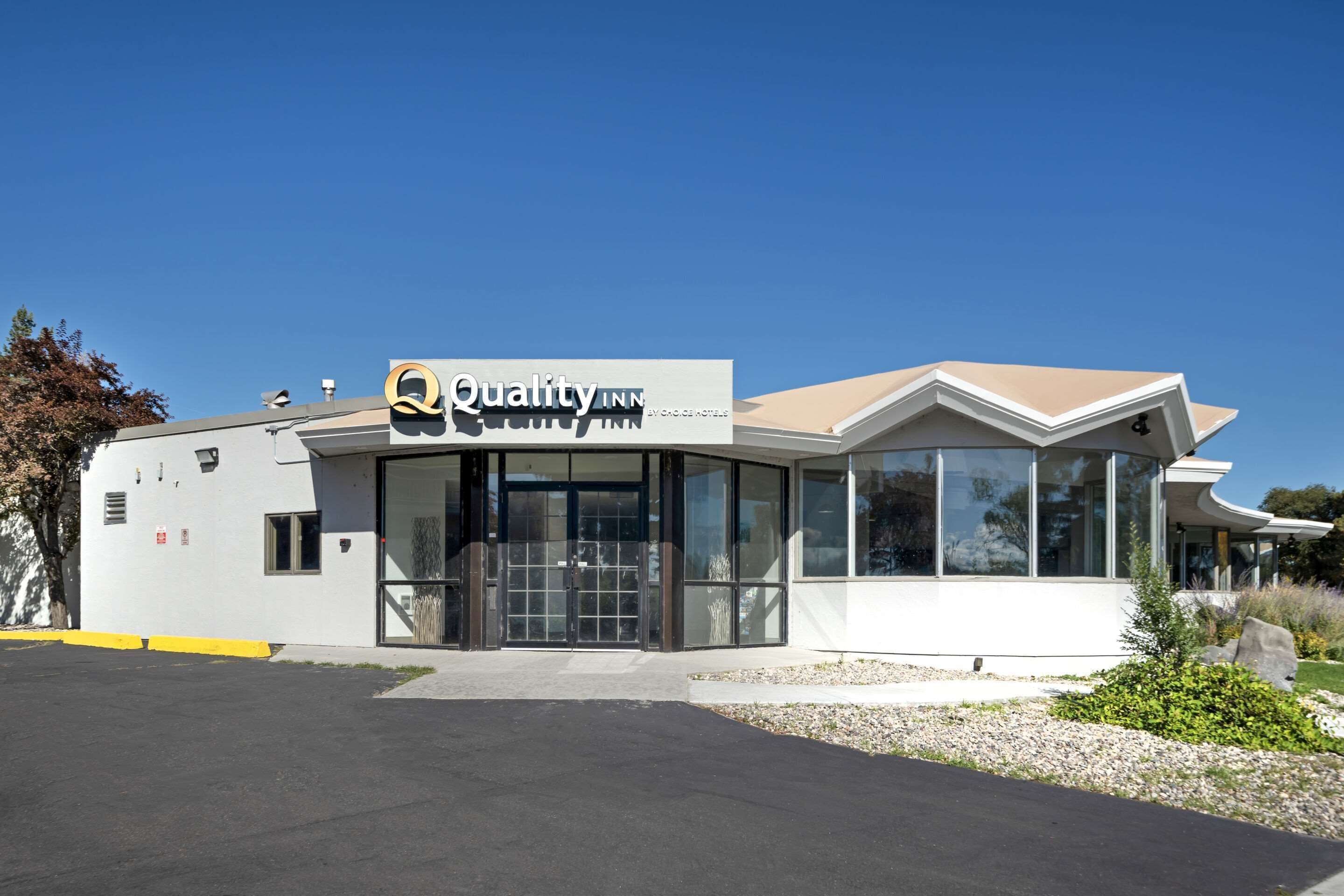 A modern building with a sign reading "Quality Inn." It features a large glass entrance, a flat roof, and a parking lot in front.