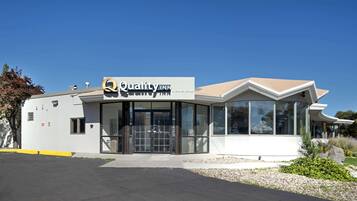 A modern building with a sign reading "Quality Inn." It features a large glass entrance, a flat roof, and a parking lot in front.