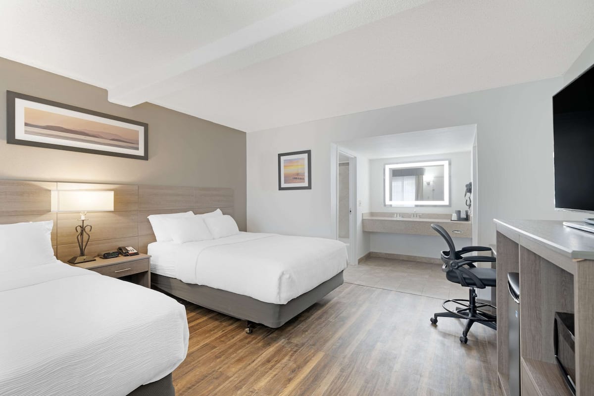 A hotel room with two beds, a desk, a chair, a TV, and a bathroom visible through an open door.