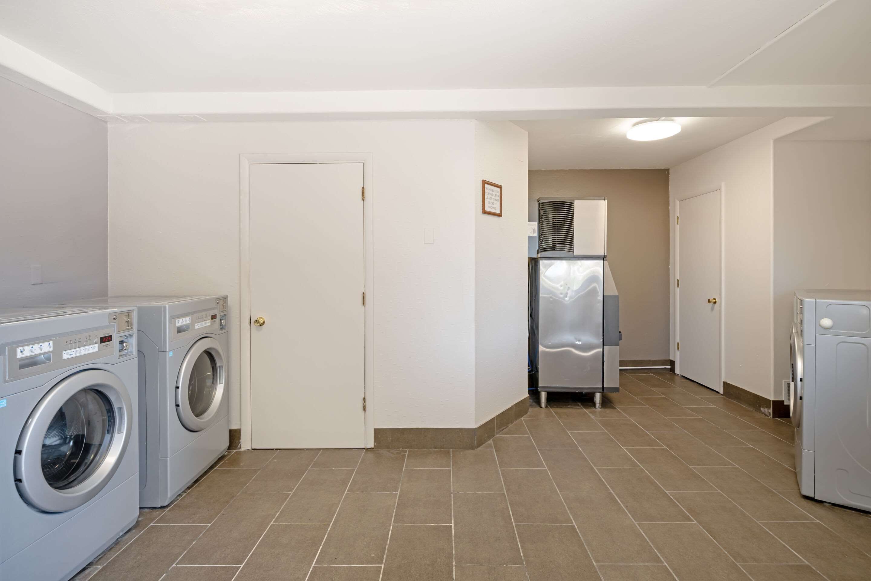 A laundry room with two front-loading washing machines, a dryer, and a refrigerator.