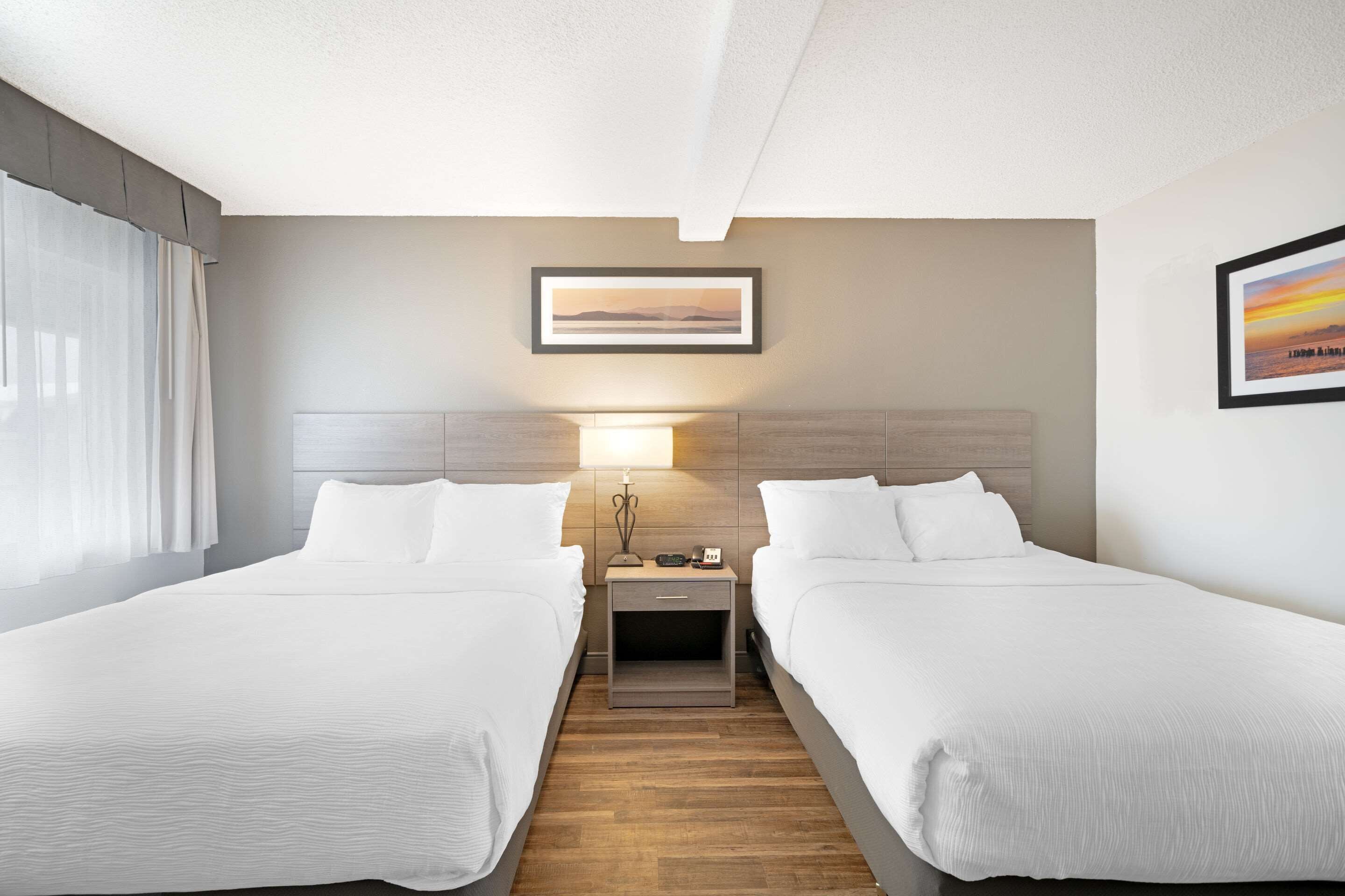 Una habitación de hotel con dos camas, una mesita de noche con lámpara y un cuadro enmarcado en la pared.