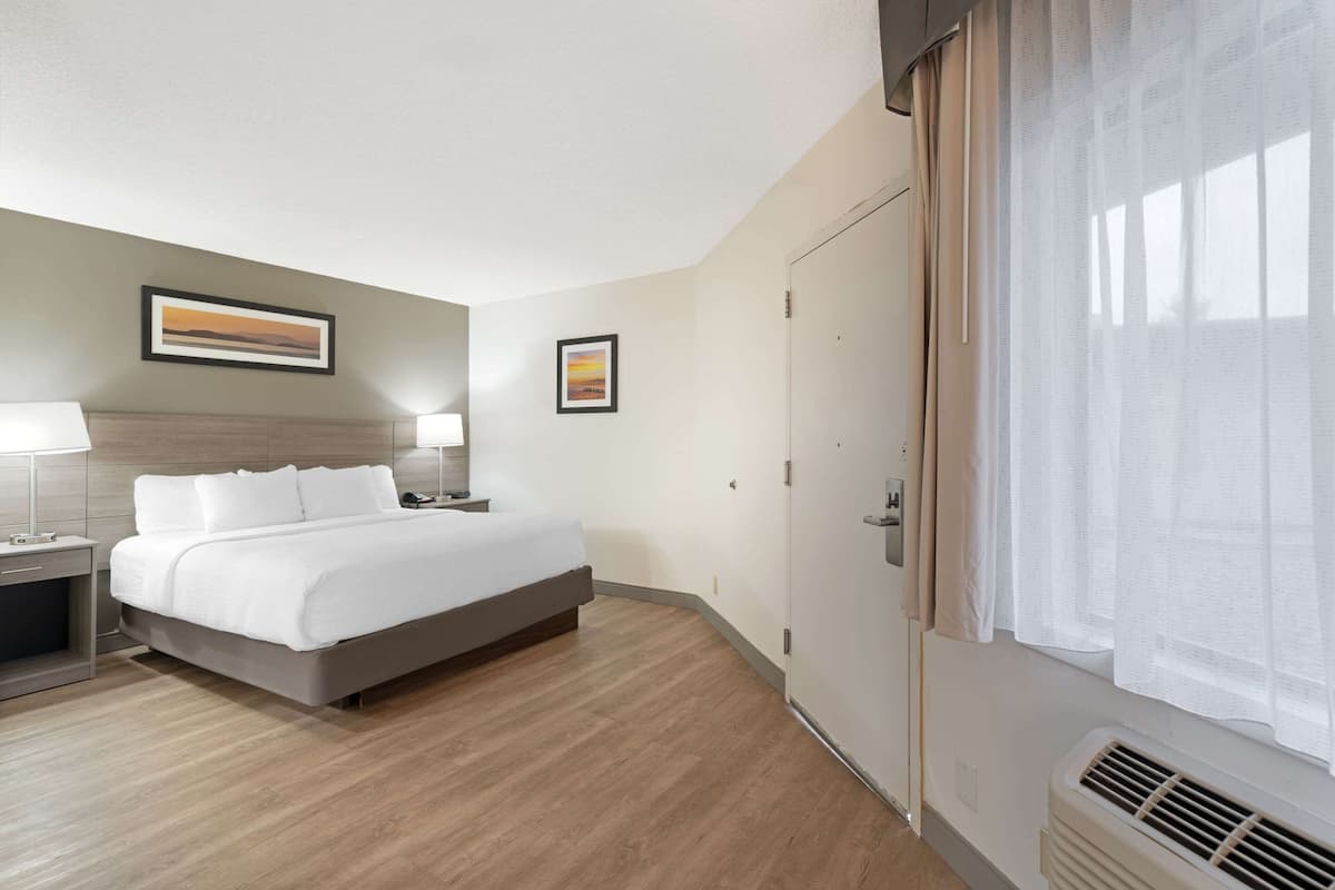 A hotel room with a bed, bedside tables, a wardrobe, and a window with sheer curtains.