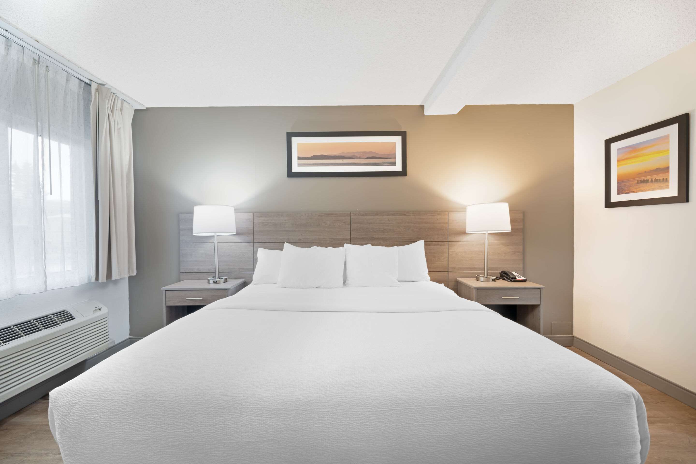 Ein Hotelzimmer mit einem großen Bett, zwei Nachttischen mit Lampen, einem gerahmten Bild an der Wand und einem Fenster mit Vorhängen.