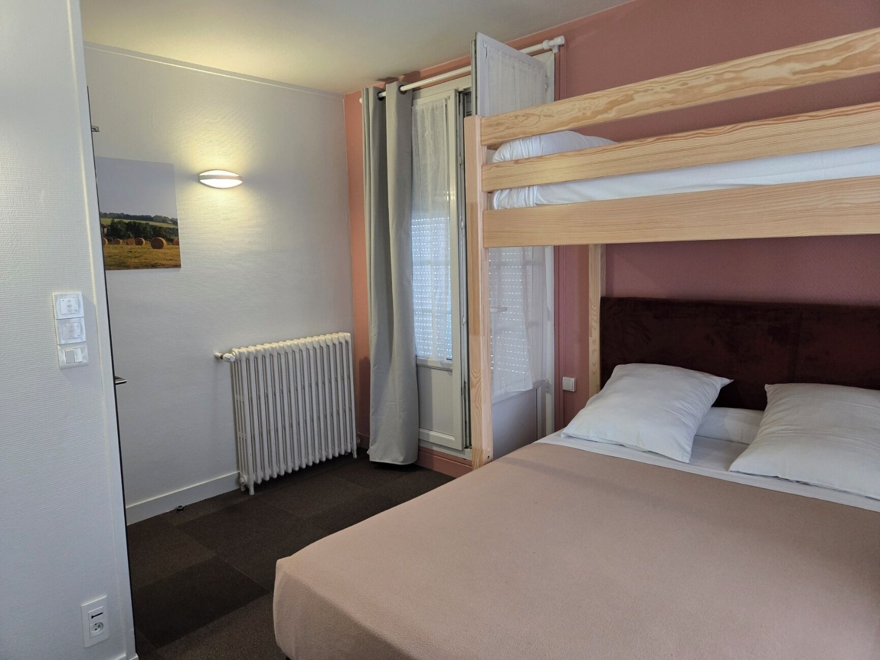 A bunk bed room with a radiator, a door with a picture, and a window with curtains.