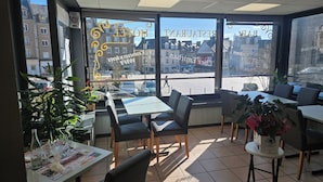 A restaurant with tables and chairs, large windows with a view of buildings, and potted plants. - Hôtel - Restaurant - Brasserie Saint Germain (Flers)