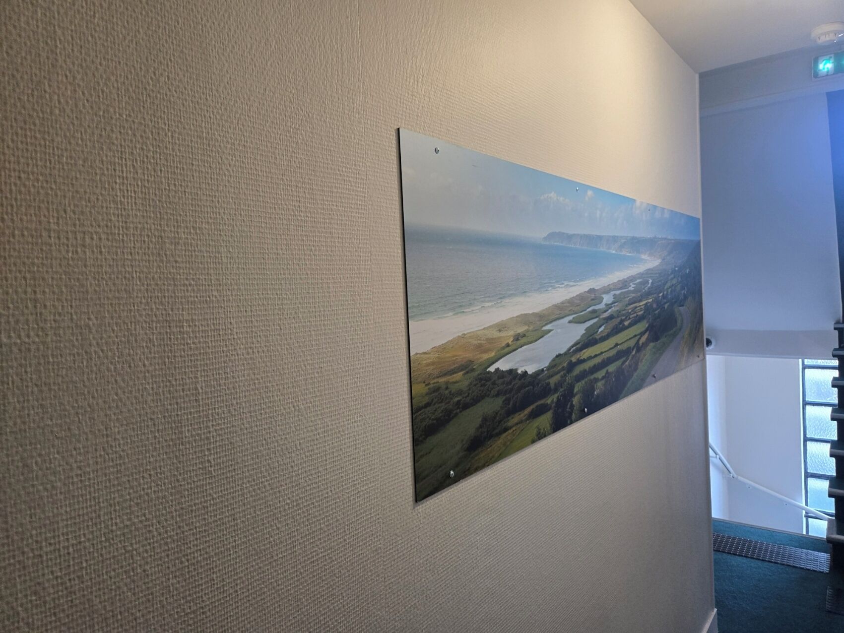 Un couloir avec un mur à texture et un tableau représentant un paysage, encadré.