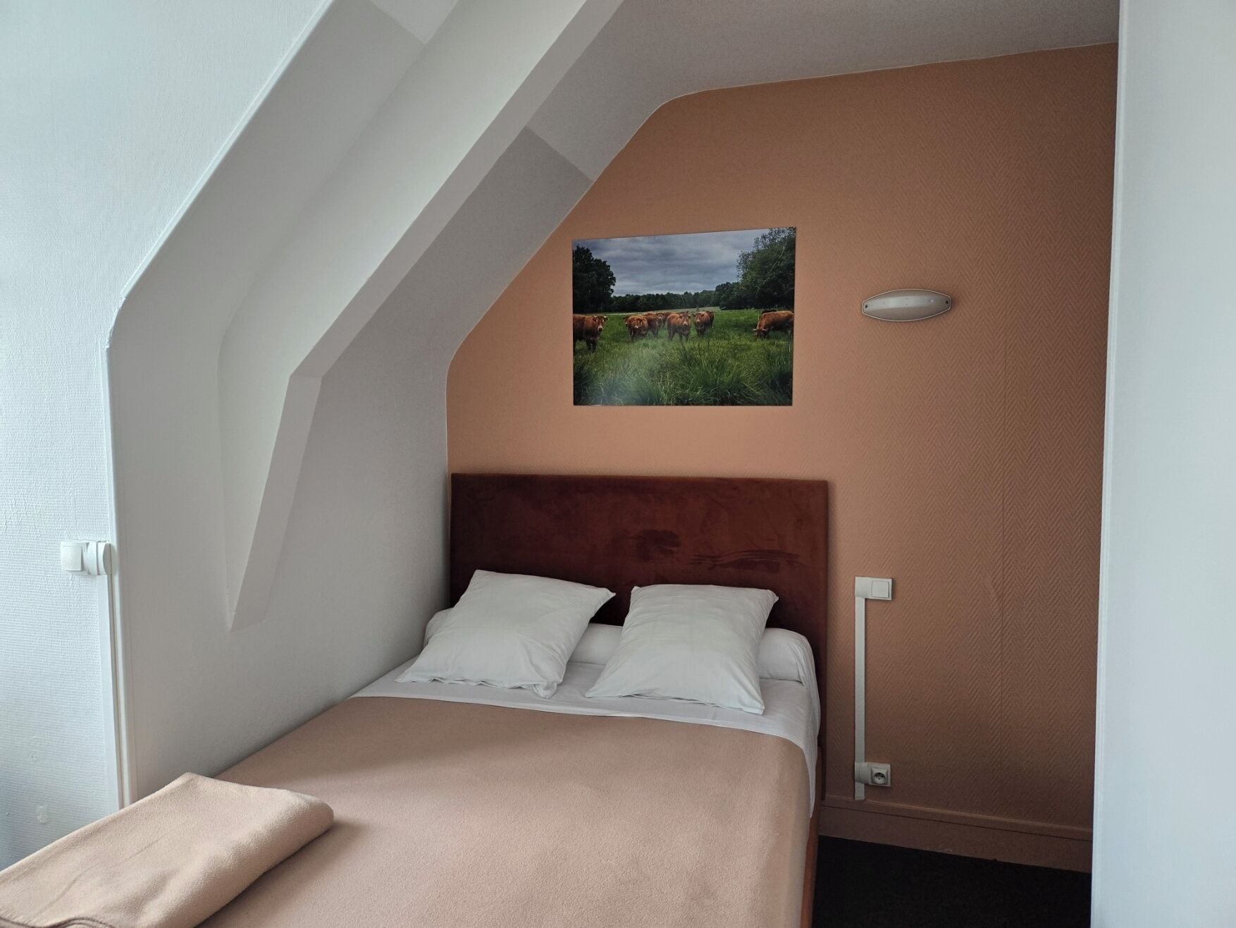 Une chambre à coucher avec un lit, une tête de lit, un tableau accroché au mur et une fenêtre.