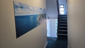 A hallway with a staircase, a wall-mounted picture of a coastal landscape, and a fire alarm. - Hôtel - Restaurant - Brasserie Saint Germain (Flers)