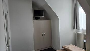 Un dormitorio con una televisión sobre un mueble, un radiador y una ventana con cortinas.