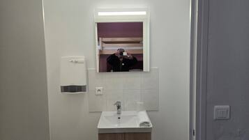 A bathroom with a white sink, mirror, and soap dispenser.