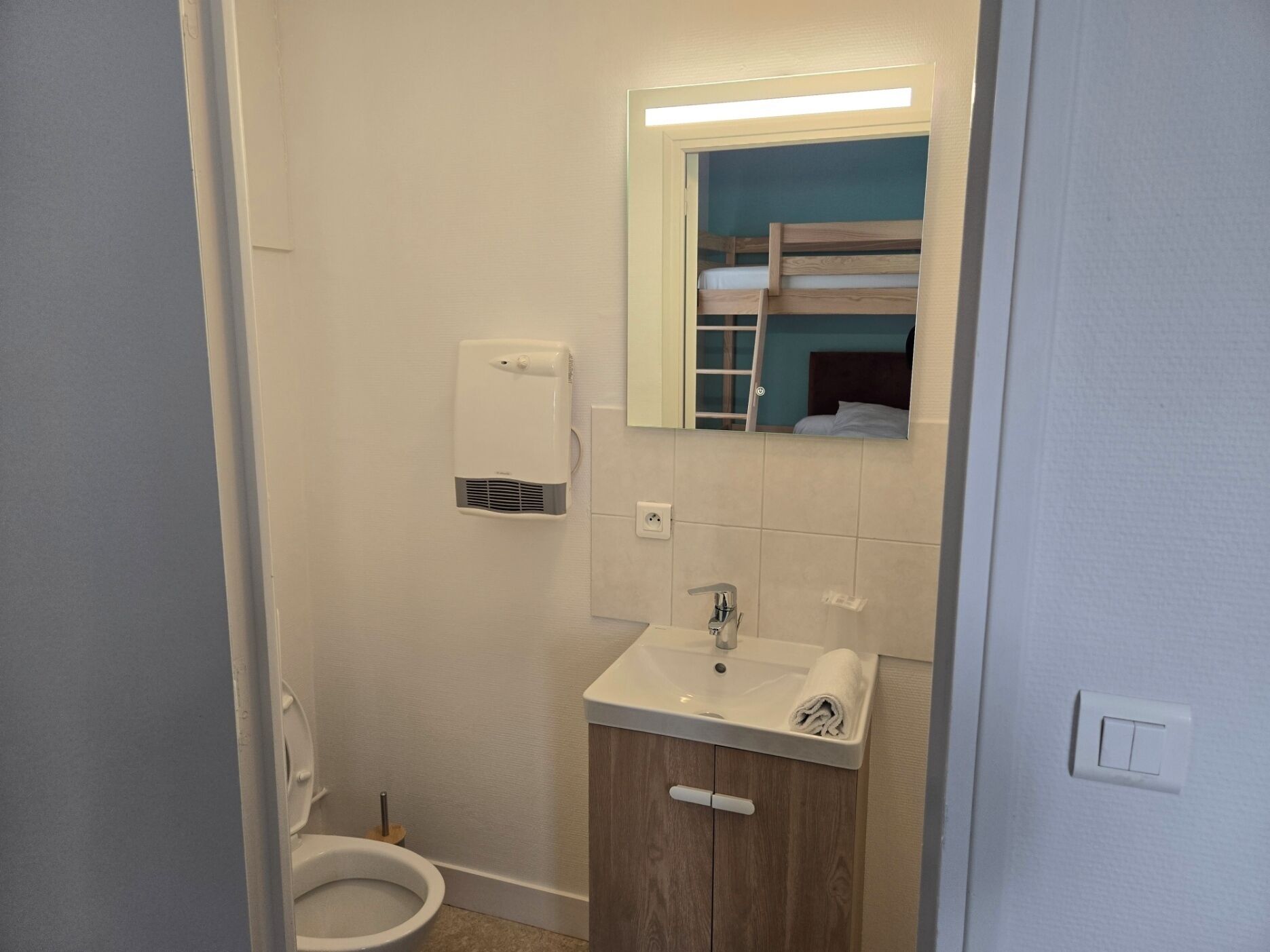 Un baño pequeño con inodoro, lavamanos, espejo y toallero.