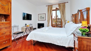 A hotel room with a wooden dresser, a bed with white linens, a small table with a chair, a TV mounted on the wall, and a window with curtains. - Terrazze Navona (Rome)